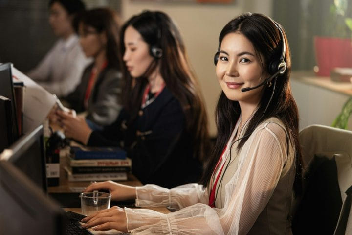 Nhạc chờ doanh nghiệp Viettel, Mobifone, Vinaphone: cách làm và mẫu lời chào Nữ tổng đài viên đeo tai nghe mỉm cười tại bàn làm việc trong trung tâm chăm sóc khách hàng