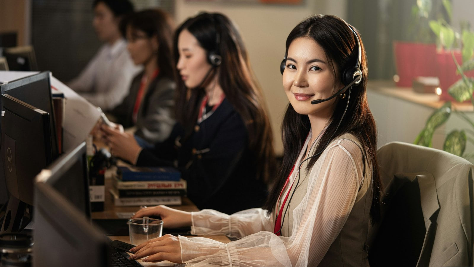 Nữ tổng đài viên đeo tai nghe mỉm cười tại bàn làm việc trong trung tâm chăm sóc khách hàng